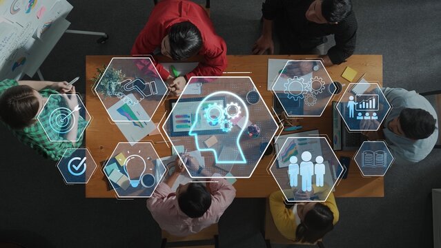 Overhead view of a team gathered around a wooden table, engaging in a brainstorming session with digital icons illustrating creativity, strategy, and teamwork. Raster