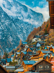 Hallstatt's beautiful wooden houses cling dramatically to a steep Alpine slope, crowned by towering, mist-covered mountains with streaks of snow and vibrant autumn foliage.