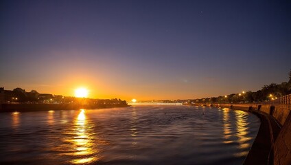 Naklejka premium Sunset over calm water with golden reflection, coastal town lights on horizon, peaceful twilight seascape with glowing sun and waterfron