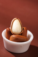 Hand-peeled pine nuts with exposed kernel in white bowl on red background