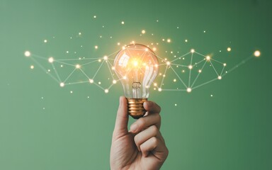 A hand holds up a classic lightbulb that glows brightly with a warm orange filament against a green background.