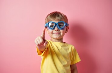 Little boy wears blue diving goggles. Smiles, points finger up to show great idea. Happy child ready for summer vacation. Kid enjoys swim fun, exploring ocean world. Youngster demonstrates new