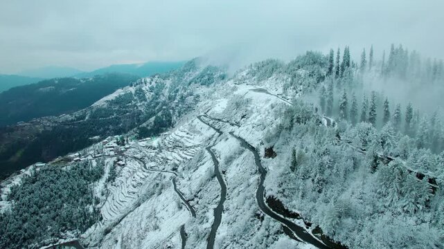 4K Aerial view of scenic snow mountain landscape with winding road and clouds. Majestic mountain view during winter season. Mountain landscape.
