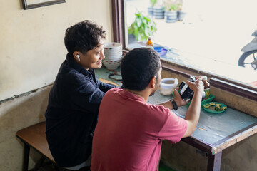 Two Indonesian Photographers Reviewing Camera Settings in a Local Cafe