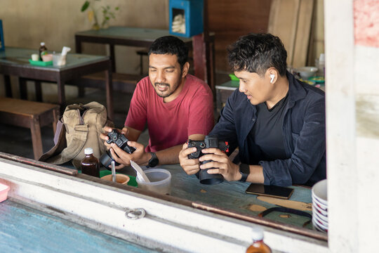 Two Indonesian Photographers Reviewing Camera Settings in a Local Cafe - Powered by Adobe