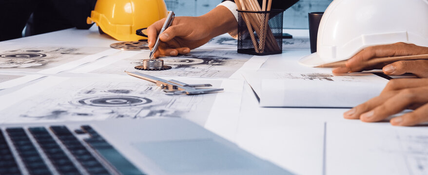 A focused team of engineers collaborates on detailed construction plans in an office environment, using safety helmets and modern technology for effective project execution. SACTR