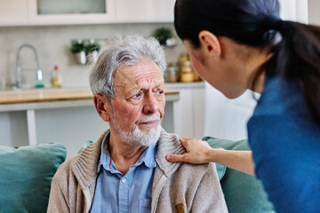 Doctor or nurse caregiver's hand giving support to sad lonely senior man at home or nursing home