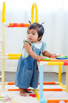 Cute asian toddler girl standing near playground structure holding colorful toys with focused expression representing concentration curiosity and early childhood motor learning