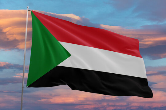 Realistic close-up of the Sudan flag waving on a tall flagpole under a bright sky with soft scattered clouds, showing smooth wind motion, vivid colors, and a strong atmosphere of national pride.
