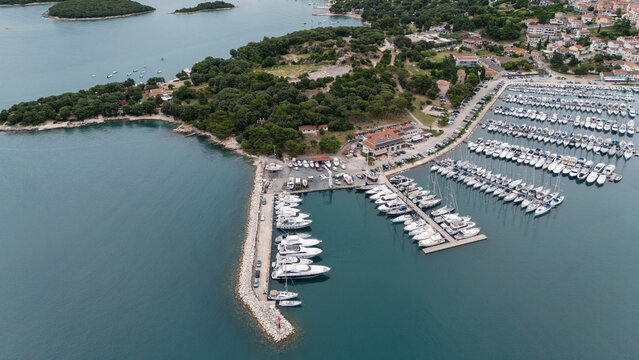 Top-down shot of a scenic harbor entrance leading to a marina filled with yachts and boats surrounded by coastal beauty