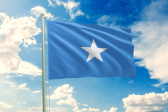Realistic close-up of the Somalia flag waving on a tall flagpole under a bright sky with soft scattered clouds, showing smooth wind motion, vivid blue colors, and a clear atmosphere of national pride.