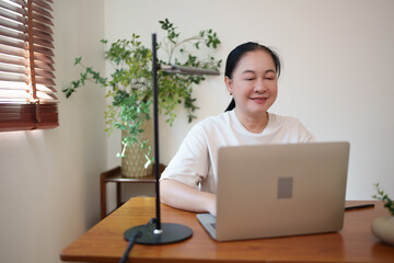 Asian middle-aged woman studying online with her laptop while listening to her lesson at home.