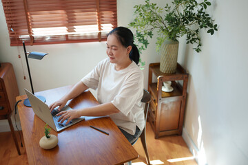 Chinese Mature woman typing on laptop at her wooden desk at her working room.