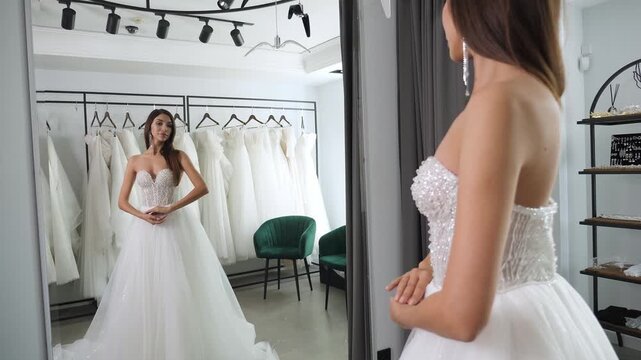 Portrait of a gorgeous woman with long hair in a beautiful wedding dress in front of a mirror in a wedding salon. A bride in a wedding dress, in a boudoir for a wedding.
