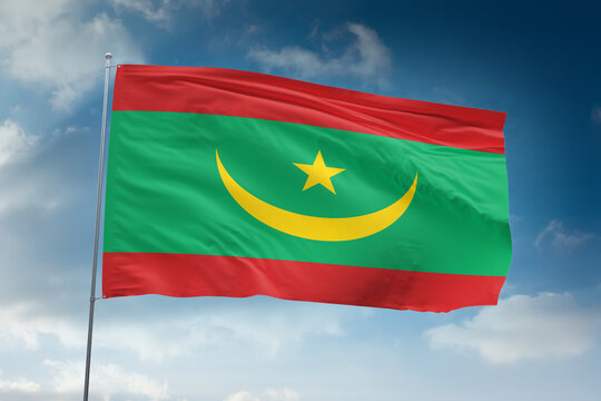 Realistic close-up of the Mauritania flag waving on a tall flagpole under a bright sky with scattered clouds, showing smooth wind motion, vivid colors, and a strong sense of national pride.
