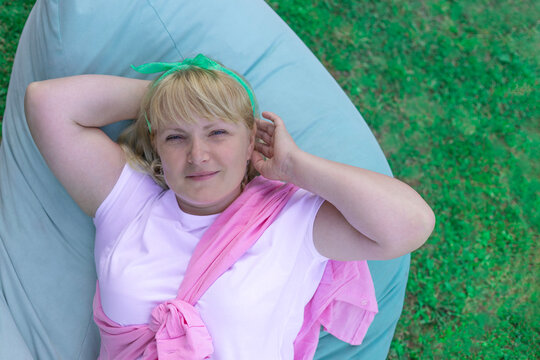 Blonde woman relaxing on a beanbag chair on the lawn, top view