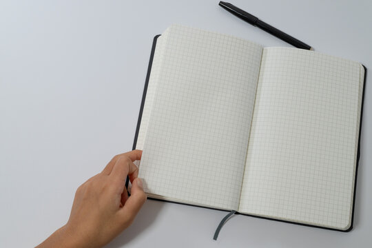 Female Hand Opening Grid Notebook on White Background - Powered by Adobe