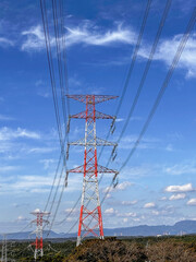 青空の下に立つ赤白の送電線鉄塔と高圧線の風景｜送電線,鉄塔,青空,インフラ