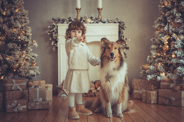 Hübsches kleines Mädchen mit Locken steht mit ihrem rough Collie  sable vor dem Weihnachtsbaum zu...