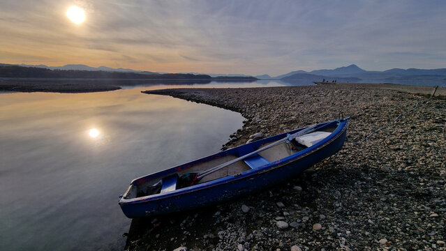 Blue boat on a rocky lake shore at sunset. - Powered by Adobe