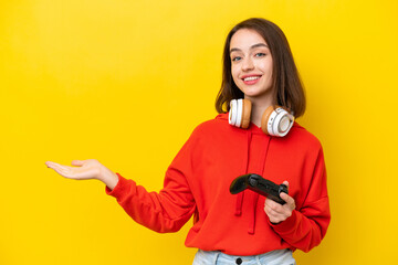 Young Ukrainian woman playing with a video game controller isolated on yellow background extending hands to the side for inviting to come