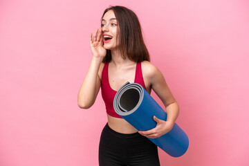Obraz premium Young sport Ukrainian woman going to yoga classes while holding a mat isolated on pink background shouting with mouth wide open to the side