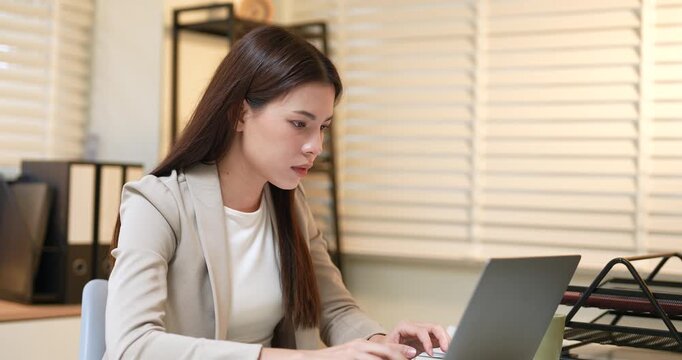 Asian businesswoman sitting at desk pressing temples with hands, feeling headache from stress and fatigue after long work hours, overworked employee suffering from mental exhaustion in office