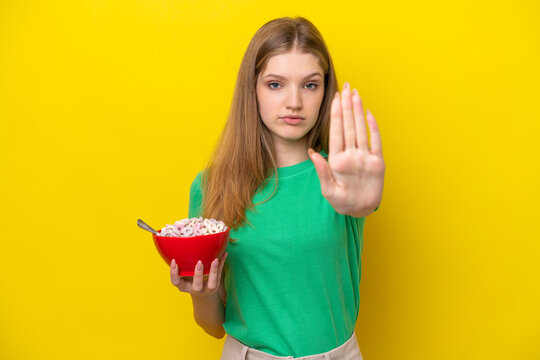 Teenager Russian girl holding bowl of cereals isolated on yellow background making stop gesture - Powered by Adobe