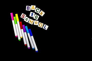 markers and letters arranged on a black background, the inscription back to school, for learning on a black magnetic board