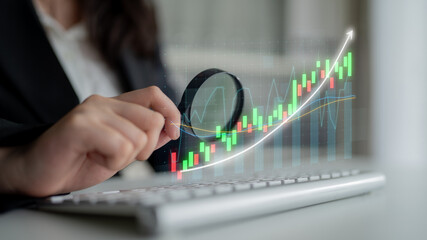 A business professional inspects stock market trends with a magnifying glass on a keyboard, highlighting digital graphs and investment opportunities in finance. Impute