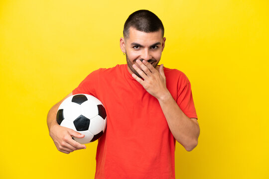 Young caucasian man playing soccer isolated on yellow background happy and smiling covering mouth with hand