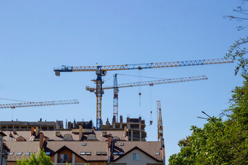 Roofs of houses and construction cranes against the blue sky