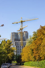 A house under construction and a construction crane among the trees. Parked cars