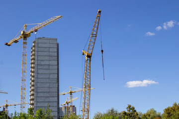 A house under construction and construction cranes against the blue sky
