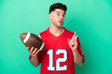 Young caucasian man playing rugby isolated on green background thinking an idea pointing the finger up