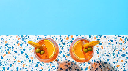 Aperol Spritz cocktails on terrazzo table with bright blue background.