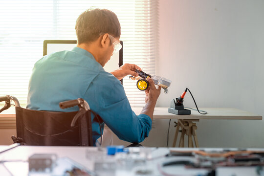 Asian engineer in wheelchair building a robot prototype in modern office