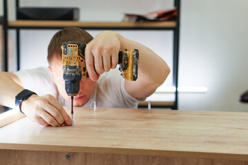 Man using cordless drill to assemble wooden furniture in workshop
