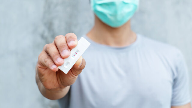 Man holding an antigen test kit on a gray background.