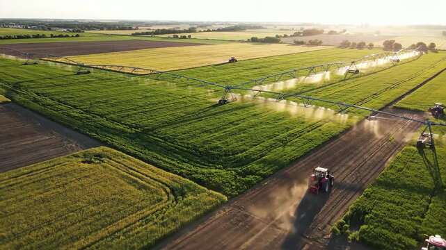 Aerial view of tractors tilling and center pivot irrigation watering vast agricultural fields at sunset
