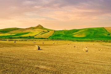 beautiful summer golden field among green hills and mountains with yellow hay stacks and scenic landscape on background. Agricultural landscape of rustic farmland.
