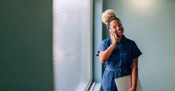 Smiling young professional woman on a phone call holding a laptop