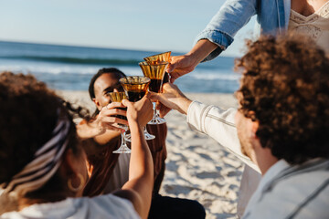 Friends toasting drinks on a beach with warm sunlight in the background