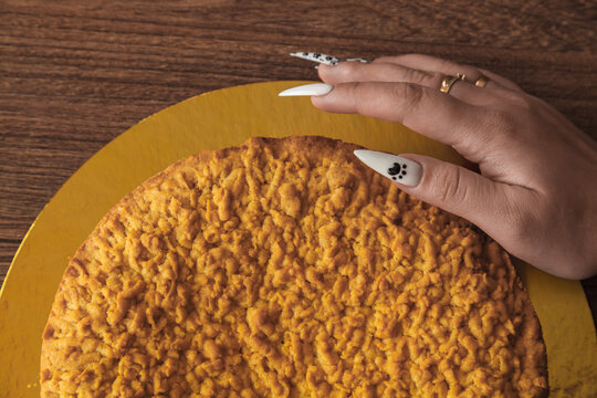 A person's hand is resting on a yellow cake. The cake is on a yellow plate. - Powered by Adobe