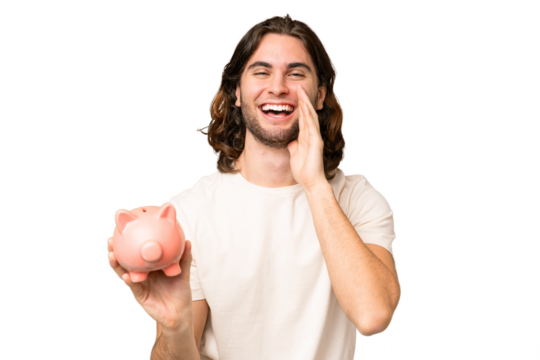 Young handsome man holding a piggybank over isolated background shouting with mouth wide open