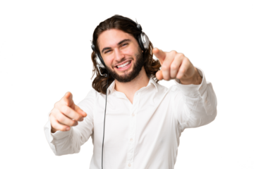 Telemarketer man working with a headset over isolated chroma key background points finger at you while smiling