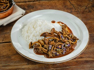 A plate of flavorful meat and mushrooms sits beside a mound of fluffy white rice. The setting is warm and inviting, showcasing a cozy meal among friends or family