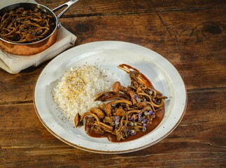 Tender pieces of meat are elegantly arranged with savory sauce and accompanied by fluffy steamed rice. The setting features a warm wooden table, adding to the inviting atmosphere