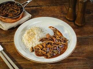 Delicious beef stew accompanied by tender white rice, garnished with herbs, set against a rich wooden backdrop that evokes warmth and comfort