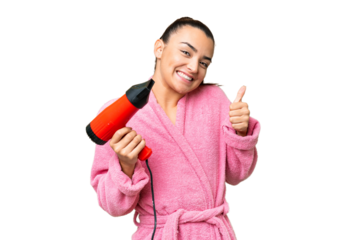 Young woman in a bathrobe holding a hairdryer over isolated chroma key background with thumbs up because something good has happened